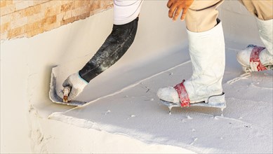 Worker wearing spiked shoes smoothing wet pool plaster with trowel