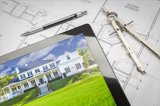Computer tablet showing finished house sitting on house plans with pencil and compass
