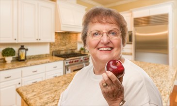 Happy senior adult woman with red apple inside kitchen