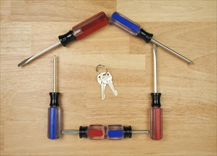 House shaped by screwdrivers and keys on a wood background