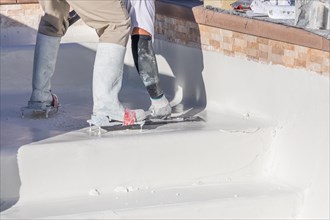 Worker wearing spiked shoes smoothing wet pool plaster with trowel