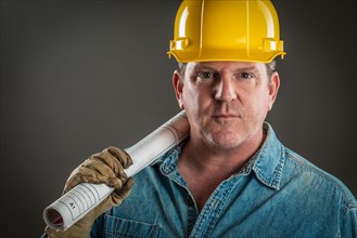 Serious contractor in hard hat holding floor plans with dramatic lighting