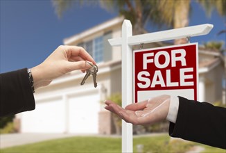 Real estate agent handing over the house keys in front of a beautiful new home and for sale real estate sign