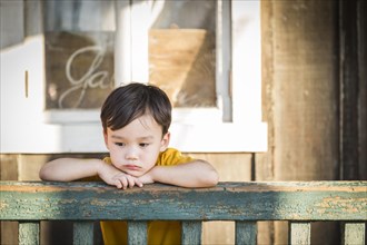 Melancholy mixed-race boy leaning on porch railing