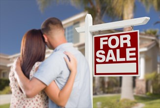 For sale real estate sign and military couple looking at nice new house