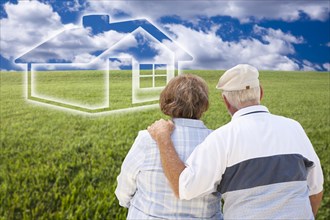 Loving senior couple standing in grass field looking over at ghosted house on the horizon