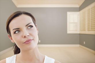 Attractive daydreaming young woman in empty grey room
