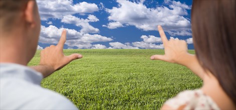 Couple framing hands around space in grass field and sky on the horizon