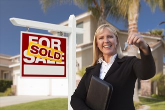 Female real estate agent handing over the house keys in front of a beautiful new home and real estate sign
