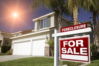 Red foreclosure for sale real estate sign in front of house with red star-burst in sky