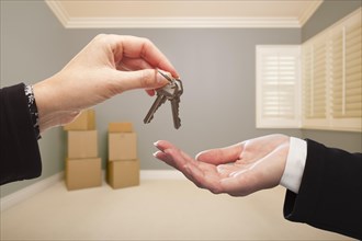 Woman handing over the house keys to A new home inside empty grey colored room