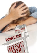 Woman with head in hand behind model home and foreclosure real estate sign in front