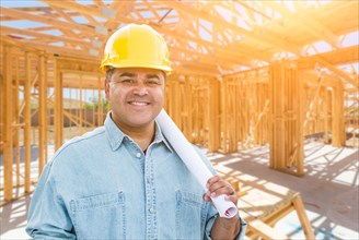 Hispanic male contractor with blueprint plans wearing hard hat at construction site