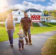 Happy mixed-race family walking in front of home and for rent real estate sign