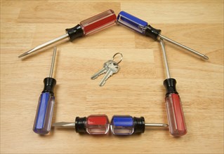 House shaped by screwdrivers and keys on a wood background