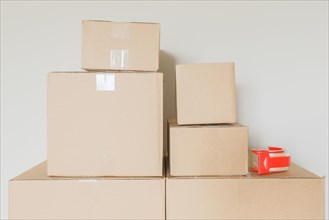 Variety of packed moving boxes and tape gun in empty room against wall