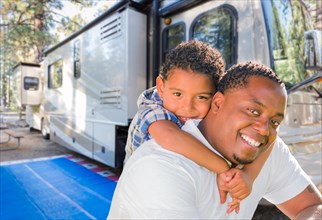 African american father with mixed-race son in front of their beautiful RV at the campground