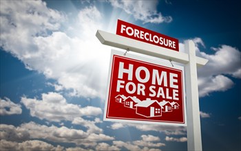 Red foreclosure home for sale real estate sign over beautiful clouds and blue sky