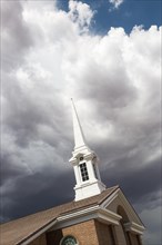 Church steeple tower below ominous stormy thunderstorm clouds