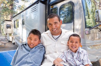 Happy hispanic father and sons in front of their beautiful RV at the campground