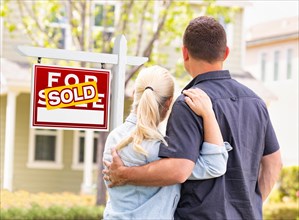 Caucasian couple facing front of sold real estate sign and house