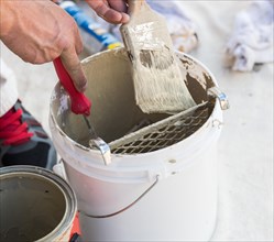 Professional painter loading paint onto his brush from A bucket