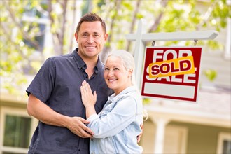 Caucasian couple in front of sold real estate sign and house