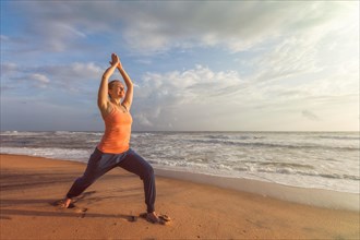 Woman doing Hatha yoga asana Virabhadrasana 1 Warrior Pose outdoors on ocean beach on sunset. Kerala