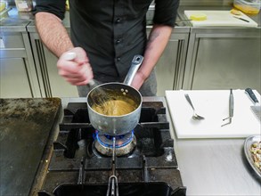 Chef using a hand mixer making a potato sauce cream reduction in a professional kitchen of a restaurant