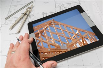 Hand of architect on computer tablet showing home framing photo over house plans