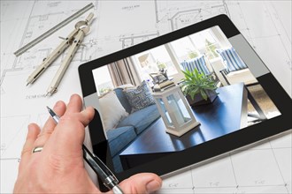 Hand of architect on computer tablet showing home interior photo over house plans