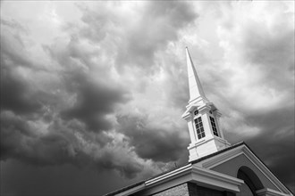 Black and white church steeple tower below ominous stormy thunderstorm clouds