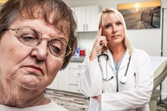 Empathetic doctor standing behind troubled senior adult woman in office