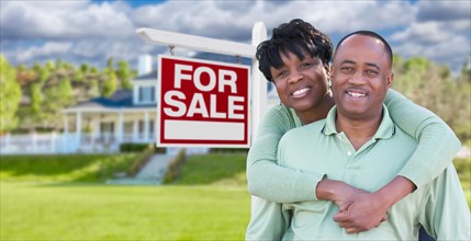 Happy african american couple in front of beautiful house and for sale real estate sign