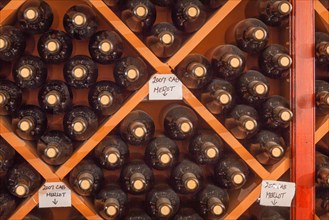 Several varietal wine bottles age on shelf inside dark cellar