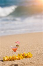 Tropical drink and lei on a sandy beach shoreline