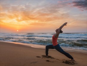 Woman doing Hatha yoga asana Virabhadrasana 1 Warrior Pose outdoors on ocean beach on sunset. Kerala