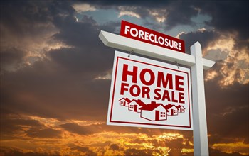 White and red foreclosure home for sale real estate sign over beautiful clouds and sunset sky