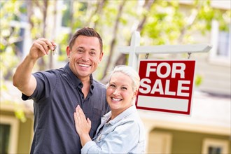 Caucasian couple in front of for sale real estate sign and house with keys