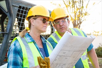 Male and female workers with technical blueprints talking at construction site