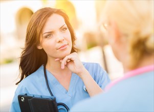 Two young adult professional female doctors or nurses talking outside
