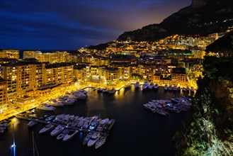 Aerial view of Monaco Monte Carlo harbour and illuminated city skyline in the evening blue hour twilight. Monaco Port night view with luxurious yachts