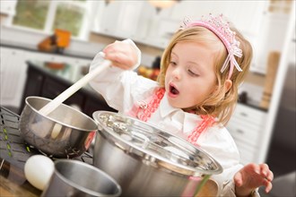 Cute baby girl playing cook with pots and pans in kitchen