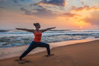 Woman doing Hatha yoga asana Virabhadrasana 1 Warrior Pose outdoors on ocean beach on sunset. Kerala