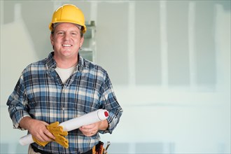 Contractor with plans and hard hat in front of drywall