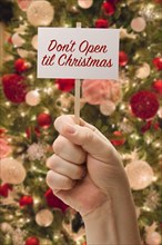 Hand holding don't open til christmas card in front of decorated christmas tree