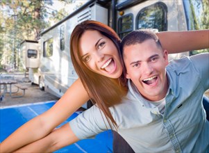 Happy caucasian couple in front of their beautiful RV at the campground