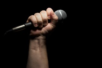 Microphone clinched firmly in male fist on a black background