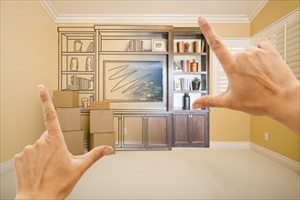 Hands framing drawing of entertainment unit gradating into photograph in room with moving boxes