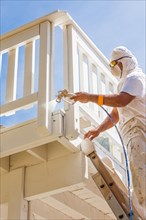Professional house painter wearing facial protection spray painting deck of A home